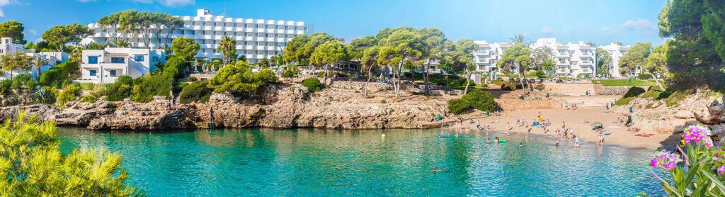 large white hotel on the rocks next to a cove with green foliage and purple flowers