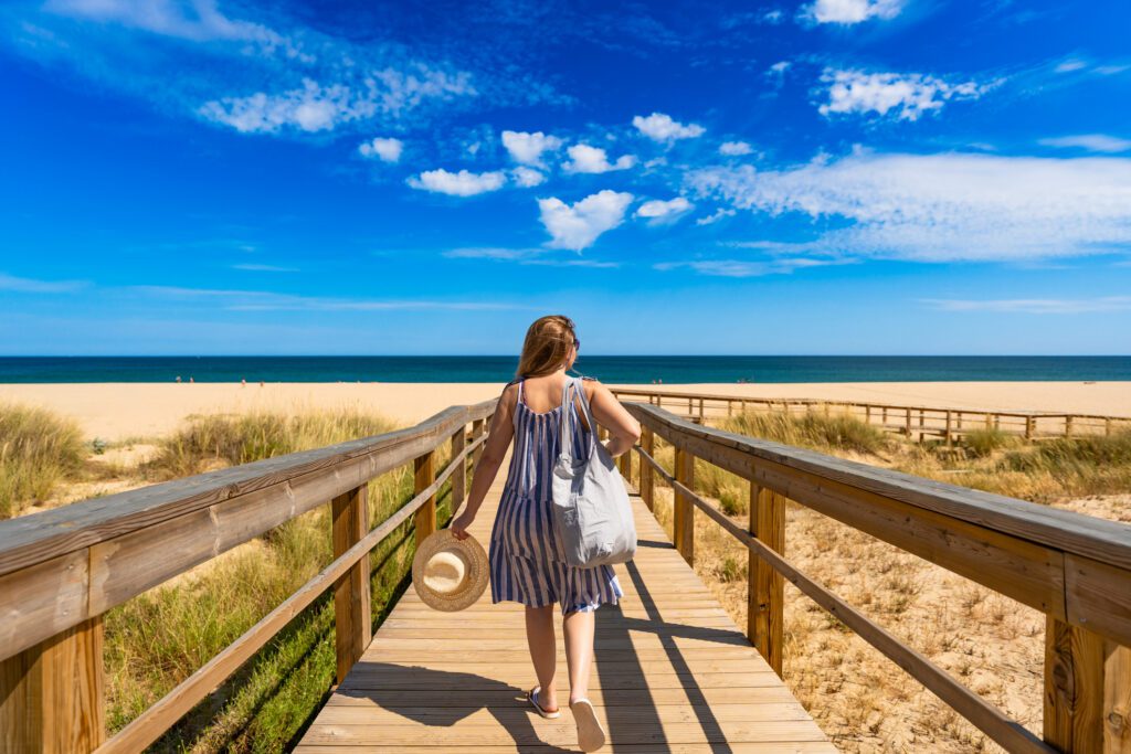 women walking on a wooden boardwalk towards a beach