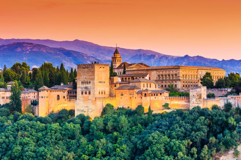 sunset orange sky with vivid mountains behind the grand yellow stone of the Alhambra Palace