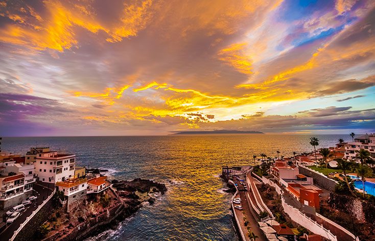 a picture from the land looking out to sea at sunset, the entire sky is yellow, orange and purple in colour