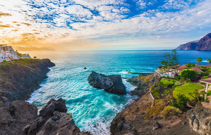 a small cove in Puerto Santiago with a cloudy blue sky and a hint of orange in one corner showing sunrise to the east