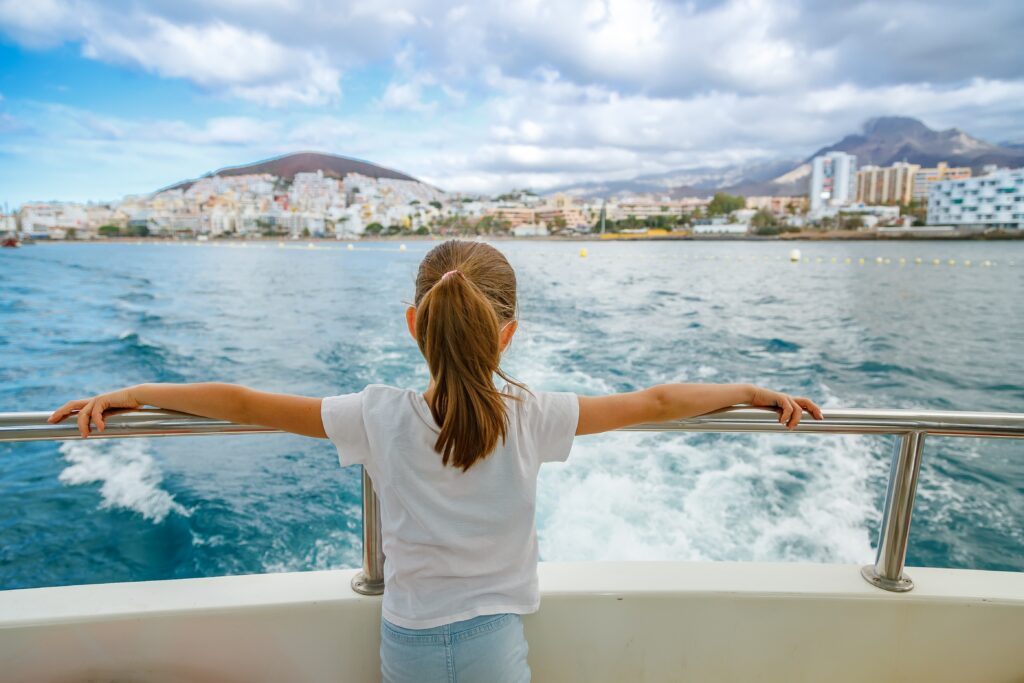 Child on the back of a boat, arms outstretched, looking out to sea